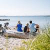 Gezin zit op het strand en kijkt uit over het water, met fietsen naast zich